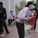 
              A woman carries a child near a line during mass testing for COVID-19 in Chaoyang district on Monday, April 25, 2022, in Beijing. China's capital Beijing began testing millions of residents and shutting down residential and business districts Monday amid a new outbreak of COVID-19. (AP Photo/Ng Han Guan)
            