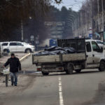 
              A man walks with a bicycle next to a truck that carries black bags with corpses of people killed during the war with Russia and exhumed from a mass grave for investigations in Bucha, in the outskirts of Kyiv, Ukraine, Monday, April 11, 2022. (AP Photo/Rodrigo Abd)
            