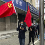 
              Residents carry the Communist Party flag and the Chinese national flag as others prepare to take part in the first round of mass COVID tests in the Jingan district of western Shanghai, China, Friday, April 1, 2022. As residents of western Shanghai start a four day lockdown for mass testing, some in eastern Shanghai about to end their lock down are being told they will be confined to their homes for at least 10 more days. It was the latest wrinkle in the lockdown of China's largest city as it struggles to eliminate an omicron-driven coronavirus outbreak under China's zero-COVID policy. (AP Photo/Chen Si)
            