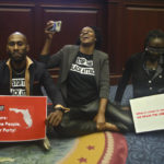 
              Rep. Tray McCurdy, D-Orlando, Rep. Angie Nixon, D-Jacksonville and Rep. Felicia Robinson, D-Miami Gardens sit on the Florida Seal in protest as debate stops on Senate Bill 2-C: Establishing the Congressional Districts of the State in the House of Representatives Thursday, April 21, 2022 at the Capitol in Tallahassee, Fla. The session was halted on the protest, but resumed later. (AP Photo/Phil Sears)
            