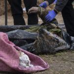 
              A policeman examines the corpse of a Ukrainian soldier removed from a mass grave in Bucha, in the outskirts of Kyiv, Ukraine, Monday, April 11, 2022. (AP Photo/Rodrigo Abd)
            