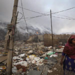 
              A ragpicker woman living on the edge of Bhalswa landfill walks past during a fire in New Delhi, India, Wednesday, April 27, 2022. The landfill that covers an area bigger than 50 football fields, with a pile taller than a 17-story building caught fire on Tuesday evening, turning into a smoldering heap that blazed well into the night. India's capital, which like the rest of South Asia is in the midst of a record-shattering heat wave, was left enveloped in thick acrid smoke. (AP Photo/Manish Swarup)
            