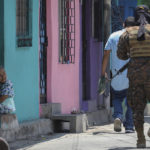 
              An elderly woman watches as soldiers patrol in the San Jose del Pino Community in Santa Tecla, El Salvador, Wednesday, April 6, 2022, during the government's unprecedented crackdown on gangs. El Salvador's congress, pushing further in the government's crackdown, has authorized prison sentences of 10 to 15 years for news media that reproduce or disseminate messages from the gangs, alarming press freedom groups. (AP Photo/Salvador Melendez)
            