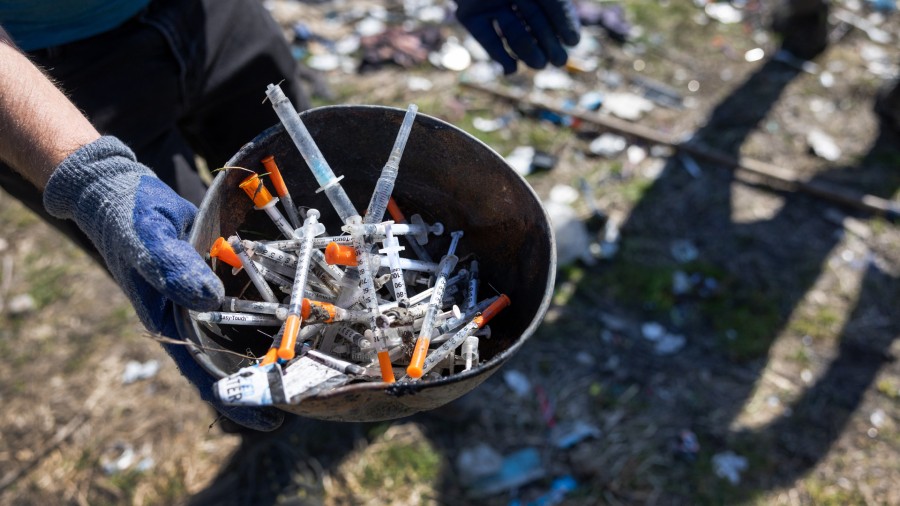 A volunteer collects heroin syringes from a homeless encampment on March 12, 2022 in Seattle, Washi...