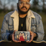 
              FILE - Adam Almonte holds a photo of him with his older brother, Fernando Morales, on a bench where they used to sit and eat tuna sandwiches after playing catch in Fort Tryon Park in New York, Wednesday, March 16, 2022. Morales died April 7, 2020 from COVID-19 at age 43. After a weekend of gun violence in America, Saturday, May 14, 2022,  when shootings killed and wounded people grocery shopping, going to church and simply living their lives, the nation marked a milestone of 1 million deaths from COVID-19. The number, once unthinkable, is now a pedestrian reality in the United States, just as is the reality of the continuing epidemic of gun violence that kills tens of thousands of people a year. (AP Photo/David Goldman, File)
            