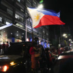 
              A supporter waves a flag as they arrive at the headquarters of Ferdinand "Bongbong" Marcos, Jr. in Mandaluyong, Philippines late Monday May 9, 2022. The son and namesake of ousted Philippine dictator Ferdinand Marcos took a commanding lead in an unofficial vote count in Monday's presidential election in the deeply divided Asian democracy. (AP Photo/Aaron Favila)
            