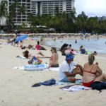 
              Brett Walsh and Emma Yates, bottom right, tourists from Australia, sit on Waikiki Beach in Honolulu, Monday, May 23, 2022. A COVID surge is under way that is starting to cause disruptions as schools wrap up for the year and Americans prepare for summer vacations. Case counts are as high as they've been since mid-February and those figures are likely a major undercount because of unreported home tests and asymptomatic infections. But the beaches beckoned and visitors have flocked to Hawaii, especially in recent months. (AP Photo/Caleb Jones)
            