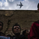 
              This photo by Los Angeles Times correspondent and photographer Marcus Yam, provided by Columbia University, shows a military transport plane flying over relatives and neighbors of the Ahmadi family, as they gather around an incinerated vehicle destroyed by a U.S. drone strike in Kabul, Afghanistan, Aug. 30, 2021. Yam was awarded the Pulitzer Prize for Breaking News Photography for work related to the fall of Kabul, in New York, Monday, May 9, 2022. (Marcus Yam/Los Angeles Times via AP)
            