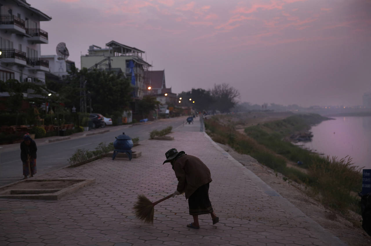 FILE - m municipal worker sweeps a pathway along the Mekong River Thursday, Dec. 12, 2013, in Vient...