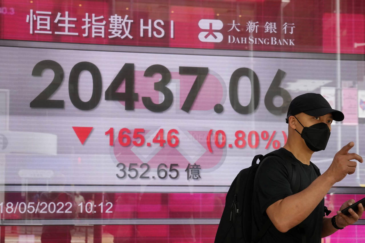 A man wearing a face mask walks past a bank's electronic board showing the Hong Kong share index in...