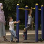 
              A woman wearing a face mask watches masked children play on a gym equipment at a public park which reopened after pandemic measure lockdown were lifted, Tuesday, May 31, 2022, in Beijing. (AP Photo/Andy Wong)
            