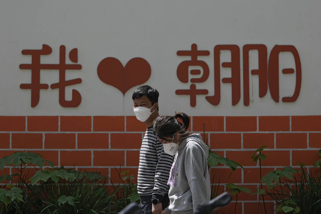 A couple wearing face masks walk by a wall displaying a words "I Love Chaoyang" as they heading to ...