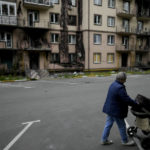 
              A woman walks with a baby stroller near a destroyed building during attacks in Irpin outskirts Kyiv, Ukraine, Monday, May 30, 2022. (AP Photo/Natacha Pisarenko)
            