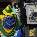 
              A supporter of Brazil's President Jair Bolsonaro look at T-shirts with images of the president, during the Labor Day and Freedom rally in Brasilia, Brazil, Sunday, May 1, 2022. (AP Photo/Eraldo Peres)
            
