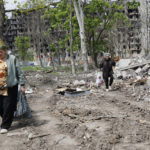
              Women walk past a destroyed apartment building in Mariupol, in territory under the government of the Donetsk People's Republic, eastern Ukraine, Monday, May 2, 2022. (AP Photo/Alexei Alexandrov)
            