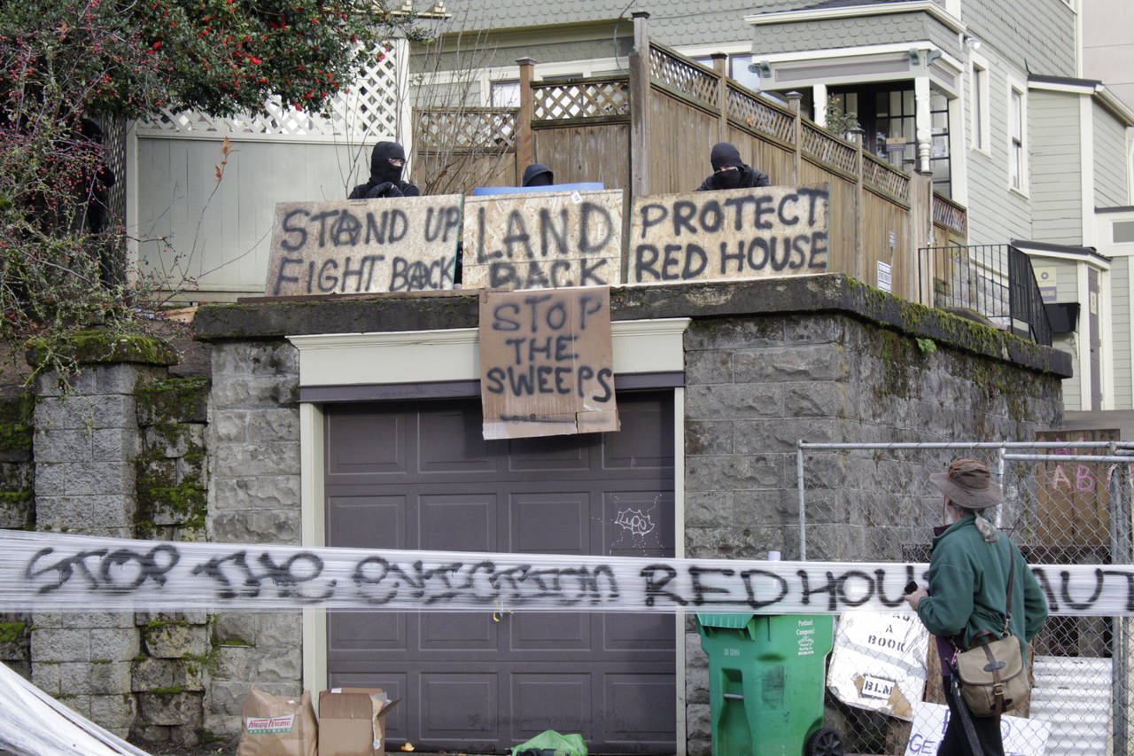 FILE - Masked protesters by an occupied home speak with a neighborhood resident opposed to their en...