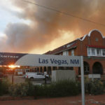 
              A sunset seen through a wall of wildfire smoke from the Amtrak train station in Las Vegas, N.M., on Saturday, May 7, 2022. The Castañeda Hotel, right, hosted meals for residents and firefighters this week with sponsorships from restaurants and other businesses. (AP Photo/Cedar Attanasio)
            