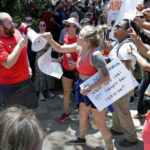 
              A counter-protester, left in red, is shouted down and has his megaphone taken away by rally attendees for pro-gun control efforts at Discovery Green Park, across the street from the National Rifle Association Annual Meeting at the George R. Brown Convention Center Friday, May 27, 2022, in Houston. (AP Photo/Michael Wyke)
            