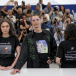 
              Producers Darya Bassel, left, and Yelizaveta Smith, right, wearing t-shirts that have an image of an explosion on the front and read "Sensitive Content: Russians kill Ukrainians. Do you find it offensive and disturbing to talk about this genocide?" pose with director Maksym Nakonechnyi who wears a t-shirt that reads "Free Tayra" in reference to Julia Paevska, aka Tayra, a Ukrainian medic who Russian forces have taken captive at the photo call for the film 'Butterfly Vision' at the 75th international film festival, Cannes, southern France, Wednesday, May 25, 2022. (AP Photo/Daniel Cole)
            