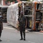 
              Sri Lankan soldiers stand guard next to burnt buses a day after clashes between government supporters and anti-government protesters in Colombo, Sri Lanka, Tuesday, May 10, 2022. Defying a nationwide curfew in Sri Lanka, several hundred protesters continued to chant slogans against the government Tuesday, a day after violent clashes saw the resignation of the prime minister who is blamed, along with his brother, the president, for leading the country into its worst economic crisis in decades. (AP Photo/Eranga Jayawardena)
            