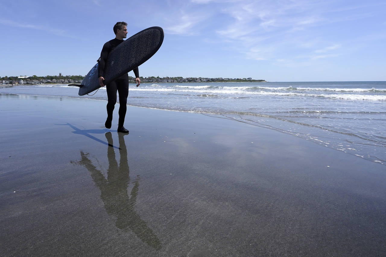 Dan Fischer, of Newport, R.I., carries his surfboard on Easton's Beach, in Newport, Wednesday, May ...