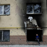 
              A boy sits on a window of a building destroyed during attacks in Irpin outskirts Kyiv, Ukraine, Monday, May 30, 2022. (AP Photo/Natacha Pisarenko)
            