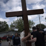 
              Dan Beazley, right, with his son Joey Beazley, from Detroit, carry a wooden cross as they pray at a memorial outside Robb Elementary School days after a deadly school shooting in Uvalde, Texas, Monday, May 30, 2022. In a town as small as Uvalde, even those who didn't lose their own child lost someone. Some say now that closeness is both their blessing and their curse: they can lean on each other to grieve. But every single one of them is grieving. (AP Photo/Wong Maye-E)
            