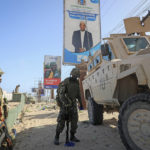 
              Ugandan peacekeepers with the African Transition Mission in Somalia (ATMIS) stand next to their armored vehicle, with a campaign poster for presidential candidate Ahmed Abdullahi Samow seen above, on a street in Mogadishu, Somalia Tuesday, May 10, 2022. Somalia is set to hold its long-delayed presidential vote on Sunday, ending the convoluted electoral process that raised tensions in the country when the president's term expired last year without a successor in place. (AP Photo/Farah Abdi Warsameh)
            