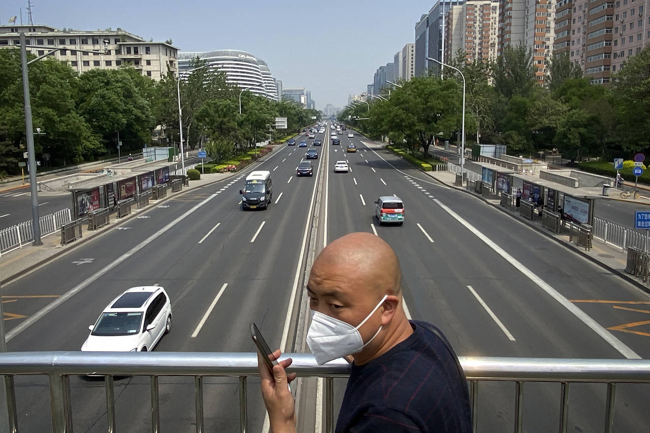 A man wearing a face mask stands on a bridge over an expressway in Beijing, Thursday, May 19, 2022....