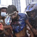 
              A Sri Lankan policeman, left, and a civilian helps an anti-government protester who was beaten up by government supporters during a clash in Colombo, Sri Lanka, Monday, May 9, 2022. Government supporters on Monday attacked protesters who have been camped outside the offices of Sri Lanka's president and prime minster, as trade unions began a “Week of Protests” demanding the government change and its president to step down over the country’s worst economic crisis in memory. (AP Photo/Eranga Jayawardena)
            