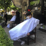 
              Barbers wearing face masks cut clients hair outside a cafe, Tuesday, May 31, 2022, in Shanghai, China. Shanghai authorities say they will take some major steps Wednesday toward reopening China's largest city after a two-month COVID-19 lockdown that has throttled the national economy and largely bottled up millions of people in their homes. (AP Photo/Chen Si)
            
