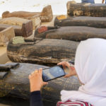 
              A reporter films painted coffins with well-preserved mummies inside, dating back to the Late Period of ancient Egypt around 500 B.C, displayed during a press conference at a makeshift exhibit at the feet of the Step Pyramid of Djoser in Saqqara, 24 kilometers (15 miles) southwest of Cairo, Egypt, Monday, May 30, 2022. (AP Photo/Amr Nabil)
            