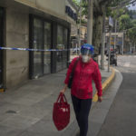 
              A woman wearing a face shield and mask walks by shophouses barricaded with caution tape Tuesday, May 31, 2022, in Shanghai, China. Shanghai authorities say they will take some major steps Wednesday toward reopening China's largest city after a two-month COVID-19 lockdown that has throttled the national economy and largely bottled up millions of people in their homes. (AP Photo/Chen Si)
            