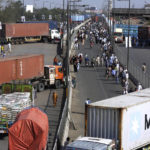 
              People walk on a highway, which block with shipping containers placed by authorities in an attempt to foil a planned rally, in Lahore, Pakistan, Wednesday, May 25, 2022. Pakistani authorities blocked off all major roads into the capital Islamabad on Wednesday, after a defiant former Prime Minister Imran Khan said he would march with demonstrators to the city center for a rally he hopes will bring down the government and force early elections.(AP Photo/K.M. Chaudary)
            