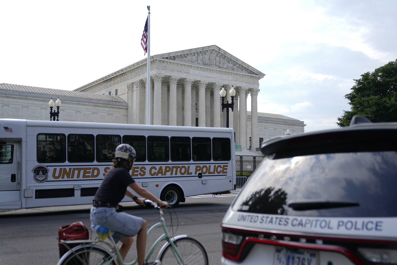 A bicyclist rides past police vehicles parked outside the U.S. Supreme Court building, Monday, June...