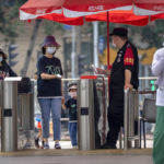 
              A security guard checks the temperature of visitors wearing face masks as they arrive at a public park on the first day of the Dragon Boat Festival holiday in Beijing, Friday, June 3, 2022, as China's capital has begun to reopen parks, shopping malls, and other places as a COVID-19 outbreak subsides. (AP Photo/Mark Schiefelbein)
            