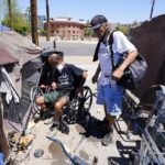 
              "Cueball", left, talks about his dog Lindsay with neighbor Terry Reed, right, at their tents Friday, May 20, 2022, in Phoenix. Hundreds of homeless people die in the streets each year from the heat, in cities around the U.S. and the world. The ranks of homeless have swelled after the pandemic and temperatures fueled by climate change soar. (AP Photo/Ross D. Franklin)
            