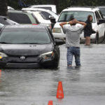 
              A driver climbs out of his stalled car after he tried to move it to higher ground from the flooded parking lot at the Beachwalk at Sheridan Apartments in Dania Beach, Fla., on Saturday, June 4, 2022. (Mike Stocker/South Florida Sun-Sentinel via AP)
            