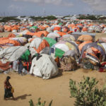 
              Somalis who fled drought-stricken areas walk next to a cluster of makeshift shelters at a camp for the displaced on the outskirts of Mogadishu, Somalia Saturday, June 4, 2022. Deaths have begun in the region's most parched drought in decades and previously unreported data show nearly 450 deaths this year at malnutrition treatment centers in Somalia alone. (AP Photo/Farah Abdi Warsameh)
            