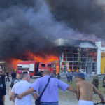 
              People watch as smoke bellows after a Russian missile strike hit a crowded shopping mall, in Kremenchuk, Ukraine, Monday, June 27, 2022. Ukrainian officials say scores of civilians are feared killed or injured after a Russian missile strike hit a crowded shopping mall in the central city of Kremenchuk. Ukrainian President Volodymyr Zelenskyy said in a Telegram post Monday that the number of victims was "unimaginable," citing reports that more than 1,000 civilians were inside at the time of the attack. (Viacheslav Priadko via AP)
            