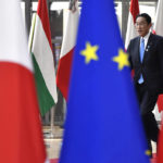 
              FILE - Japan's Prime Minister Fumio Kishida walks between flags prior to a meeting with European Council President Charles Michel at the European Council building in Brussels on March 24, 2022. Kishida, despite an underwhelming start eight months ago, is enjoying surprising popularity by playing it safe as the public's worries about the coronavirus and global conflicts ease. (AP Photo/Geert Vanden Wijngaert, File)
            