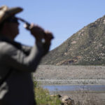 
              FILE - Samuel Santos casts into El Capitan Reservoir as he fishes near the dam, seen in background on April 8, 2022, in Lakeside, Calif. Constructed four generations ago, the massive rock and clay dam at El Capitan Reservoir is capable of storing over 36 billion gallons of water — enough to supply every resident in San Diego for most of a year. Today, it's three-quarters empty — intentionally kept low because of concerns it could fail under the strain of too much water. (AP Photo/Gregory Bull, File)
            
