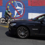 
              A man with a child rides a bicycle by a wall that shows the colours of the Serbian flag and graffiti against EU and NATO in Belgrade, Serbia, Tuesday, June 21, 2022. European Union leaders will seek to offer support this week to six Western Balkan nations that have long been knocking at the bloc's doors, and now see the war in Ukraine raging not far from their borders amid fears that Russia could turn its sights on their region. Serbia, the largest of the six countries, is pivotal in Russia's regional influence. (AP Photo/Darko Vojinovic)
            
