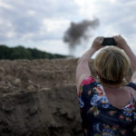 
              A journalist takes a picture of smoke rising from a landmine exploded by a Ukrainian specialized team working on a field to clean the area on the outskirts of Kyiv, Ukraine, Thursday, June 9, 2022. (AP Photo/Natacha Pisarenko)
            