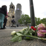 
              People walk past flowers and candles at the Kaiser Wilhelm Memorial Church in Berlin, Germany, Thursday, June 9, 2022. On Wednesday June 8, a 29-year-old man drove his car into a group of students killing their teacher and crash into a store. (AP Photo/Michael Sohn)
            