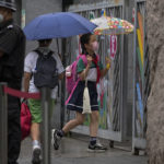 
              Students wearing face masks and holding umbrellas in the rain enter a primary school in Beijing, Monday, June 27, 2022. Primary and middle school students in the capital city returned to school on Monday after school classes being shuttered for months due to the COVID-19 controls. (AP Photo/Andy Wong)
            