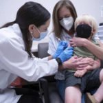 
              Pharmacist Kaitlin Harring, left, administers a Moderna COVID-19 vaccination to three year-old Fletcher Pack, while he sits on the lap of his mother, McKenzie Pack, at Walgreens pharmacy Monday, June 20, 2022, in Lexington, S.C. Today marked the first day COVID-19 vaccinations were made available to children under 5 in the United States. (AP Photo/Sean Rayford)
            