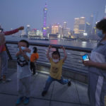 
              Children play as the Shanghai city skyline is lit near dusk along the bund, Wednesday, June 1, 2022, in Shanghai. Traffic, pedestrians and joggers reappeared on the streets of Shanghai on Wednesday as China's largest city began returning to normalcy amid the easing of a strict two-month COVID-19 lockdown that has drawn unusual protests over its heavy-handed implementation. (AP Photo/Ng Han Guan)
            