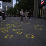 
              Pedestrians walk over yellow circles, painted by investigators to mark evidence and other items on the sidewalk of the street after a car crashed into a crowd of people in central Berlin, Germany, Wednesday, June 8, 2022.  Authorities say a teacher was killed and nine people were seriously injured after a man drove a car into a German school group standing in a popular Berlin shopping district. (AP Photo/Markus Schreiber)
            