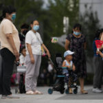 
              A child wearing a face mask throws a sand bag to a masked woman as residents bring their children play on a commercial office building compound in Beijing, Tuesday, June 28, 2022. (AP Photo/Andy Wong)
            